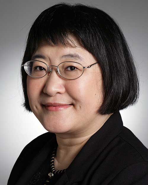 Dressed in black, before a soft gray backdrop, Chinese composer Dr. Chen Yi smiles, while looking directly at the camera.